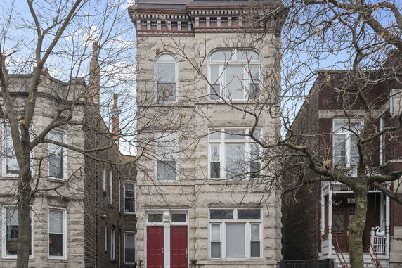 Front view of a multi-story stone house with red double doors and several large windows.