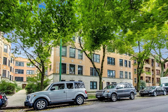 Front view of a multi-story apartment building with trees and parked cars.