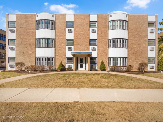 Front view of a multi-story brick apartment building with a central entrance and numerous windows.