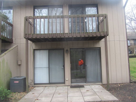Front view of a two-story house with a wooden balcony and sliding glass doors.