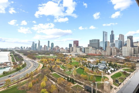 View of a city skyline with tall buildings, roads, and a park in the foreground.