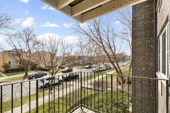 View from a balcony showing a residential street with cars parked and trees lining the sidewalk.