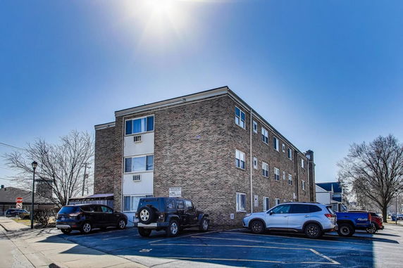Front view of a three-story brick apartment building with windows and parked cars in front.