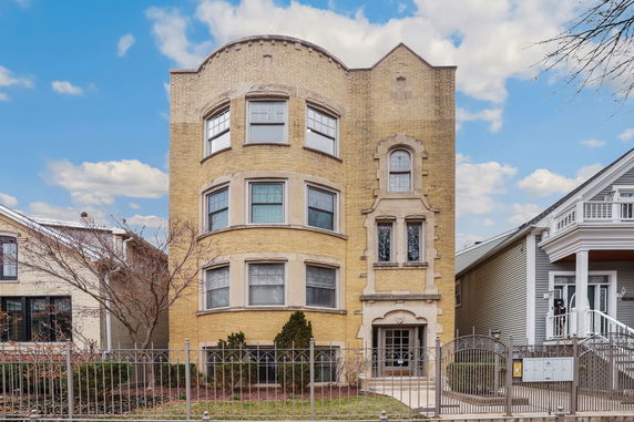 Front view of a three-story yellow brick building with bay windows.