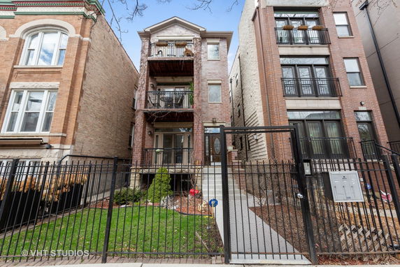 Front view of a three-story brick building with balconies and a gated entrance.