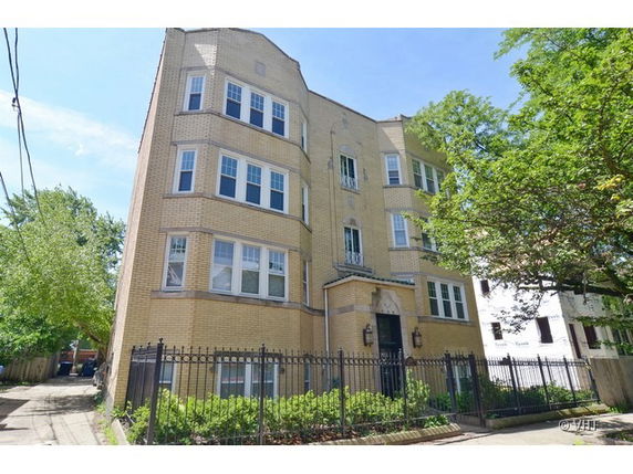 Front view of a multi-story brick building with multiple windows and a gated entrance.