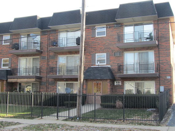 Front view of a three-story brick apartment building with balconies.