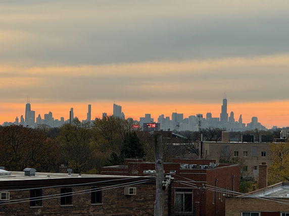 Wide angle view of a city skyline at sunset with buildings in the foreground.