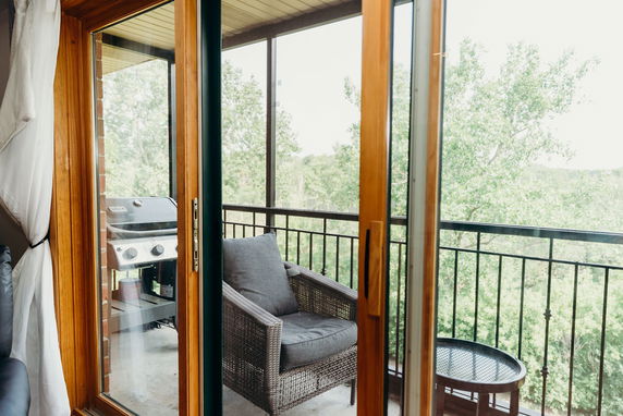View of surrounding trees from a balcony with a wicker chair and grill visible.