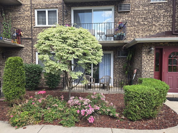 Front view of a two-story brick building with balconies and a small garden area.