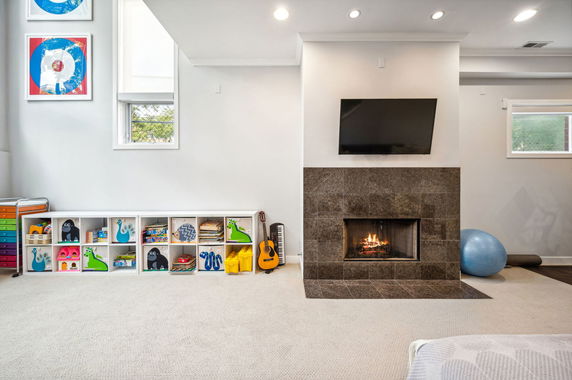 Interior view of a play area featuring a fireplace, shelves with toys, and a television.