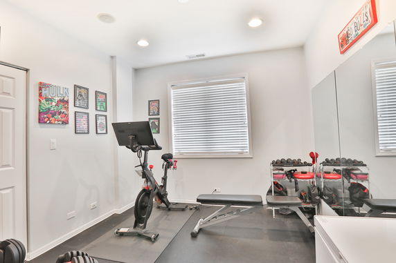 Indoor home gym with exercise bike, bench, and dumbbells.