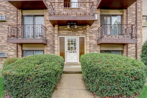 Front view of a multi-story brick building with balconies and a central entrance door.