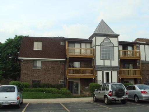 Front view of a multi-story building with balconies and a distinctive pointed roof feature.