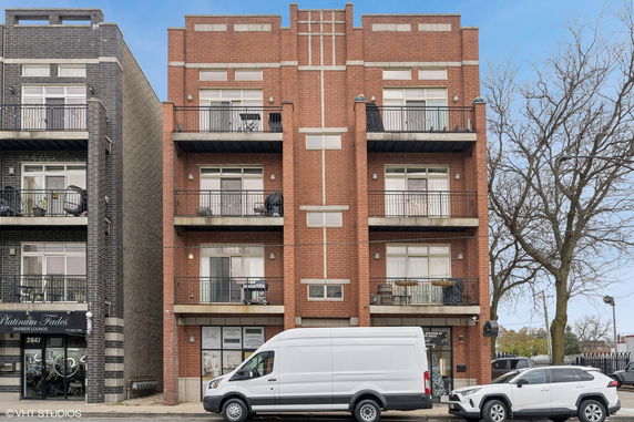 Front view of a four-story apartment building with balconies and storefronts on the ground level.
