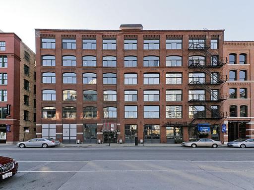 Front view of a multi-story brick building with large windows and a fire escape.