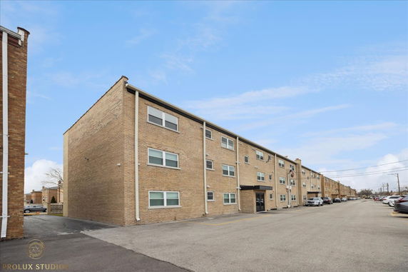Front view of a three-story brick apartment building with multiple windows and parking area.