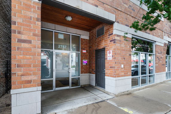 Exterior view of a multi-story building entrance with brick facade and glass doors.