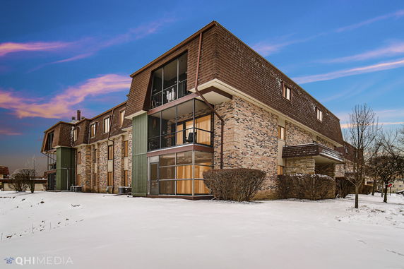 Front view of a multi-story brick building with large windows and a sloped roof.