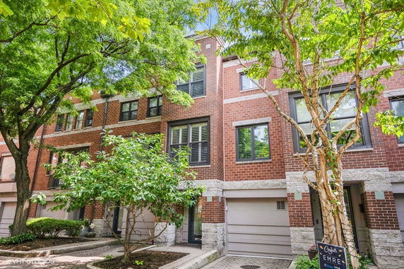 Front view of a multi-story brick townhouse with garage and trees.
