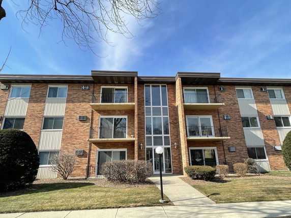 Front view of a three-story brick apartment building with balconies.