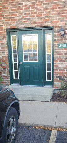 Front view of a brick building entrance with a green door and side windows.