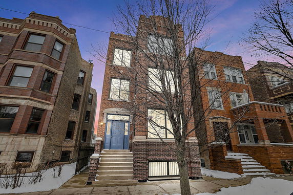 Front view of a multi-story brick building with steps leading to a blue door.