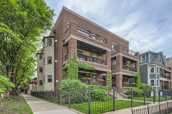Front view of a multi-story brick building with balconies and greenery.