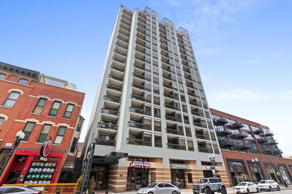 Front view of a multi-story building with balconies and street-level shops.