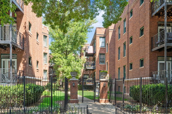 Front view of a brick apartment building with balconies and a gated entrance.