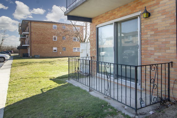 Front view of a brick apartment building with a small patio area and metal railing.