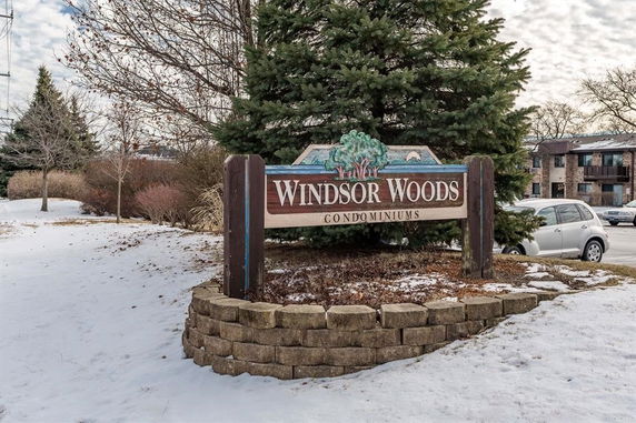 Front view of Windsor Woods condominium complex sign with nearby buildings in the background.