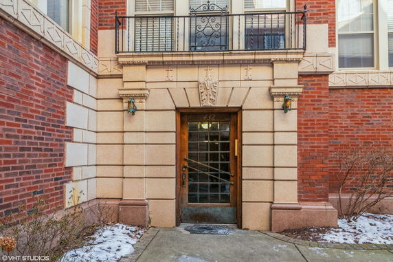 Front view of a brick building entrance with decorative stonework and a balcony.