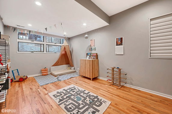 Indoor play area with wooden flooring, a play mat, toys, a small mattress with canopy, and storage shelves.