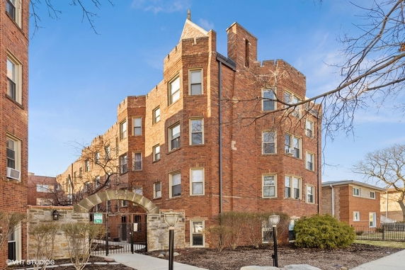 Front view of a multi-story brick apartment building with an arched entrance.