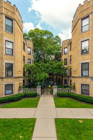 Front view of a multi-story apartment building with a central courtyard and arched entrances.