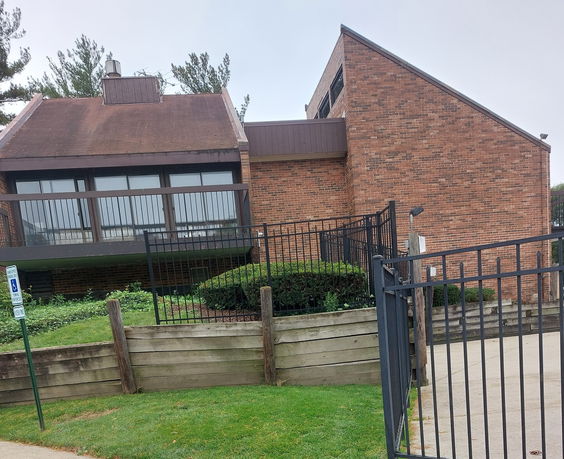 Front view of a brick building with a sloped roof and large windows.