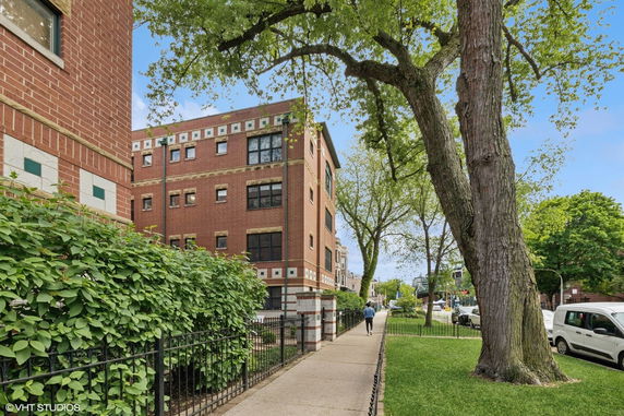 Front view of a multi-story brick building with a sidewalk and trees.