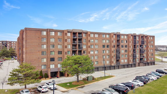 Front view of a multi-story brick apartment building with parking area.