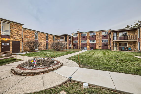 Front view of a brick apartment complex with multiple units and a central courtyard.
