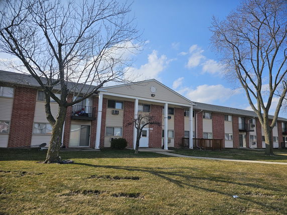 Front view of a multi-story apartment building with balconies and a brick facade.