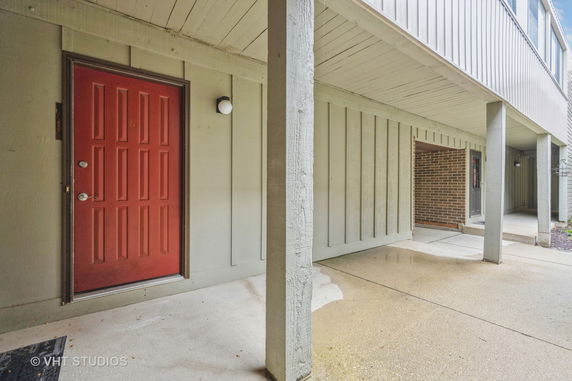 Covered entryway of a building with a red door and light-colored siding.