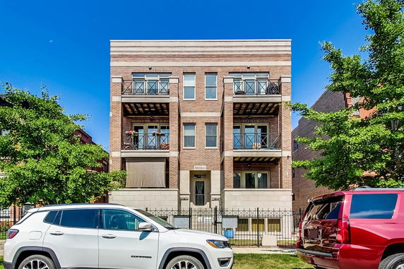 Front view of a three-story brick apartment building with balconies.
