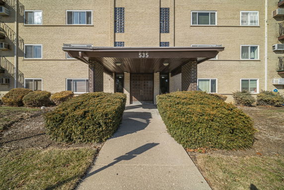 Front view of a multi-story apartment building entrance with a covered walkway.