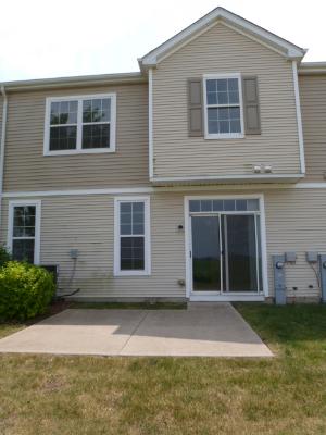 Rear view of a two-story house with beige siding and sliding glass door.