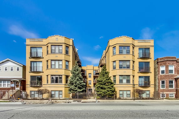 Front view of a multi-story apartment building with yellow brick facade and balconies.