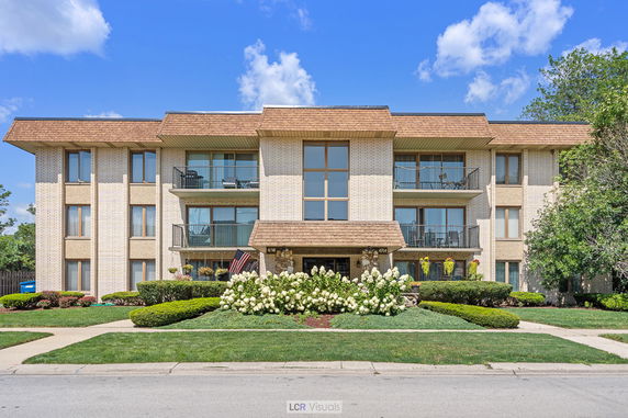 Front view of a three-story residential building with balconies and landscaped surroundings.