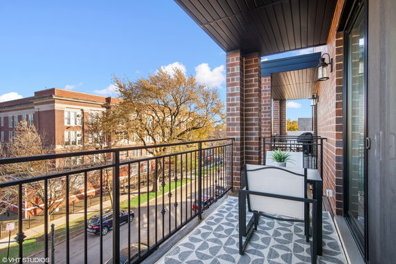 Balcony view overlooking a street with a brick building and trees.