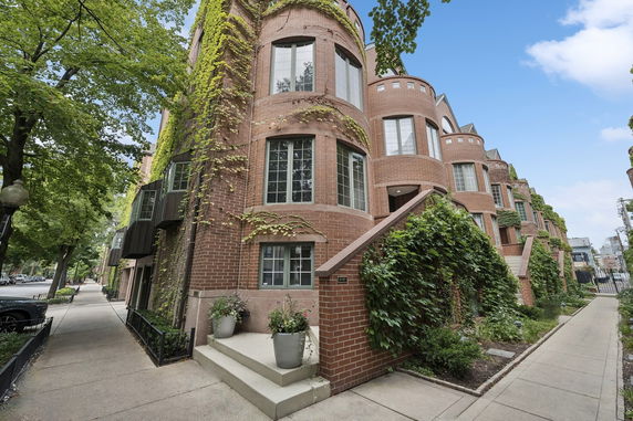 Front view of a brick building with multiple rounded sections and climbing plants.
