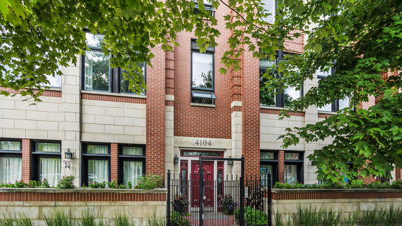 Front view of a brick house with black framed windows and a gated entrance.